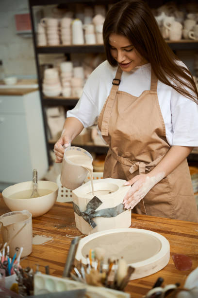 istock Smiling woman in apron pouring pottery mixture into a mold in studio 2164508644