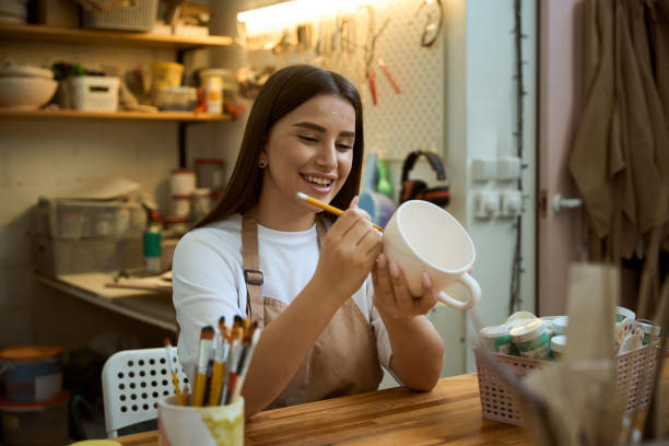 istock Smiling woman potter holding pencil and painting on clay cup 2164508708
