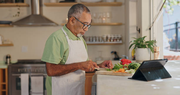 istock Home, senior man and cutting vegetables for dinner, lunch and supper preparation. Kitchen counter, male cook and healthy food with nutrition, vegan meal and tablet for recipe ingredients in house 2164514817