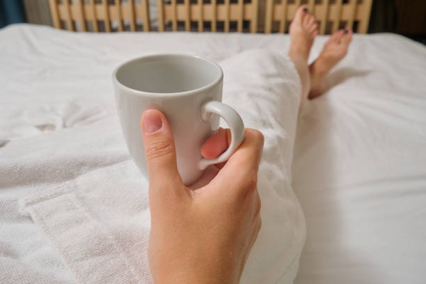 Happy woman sitting down indoors with a coffee. Focus in on the cup and hands.