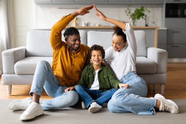 istock Black family forms house shape with hands, sitting on floor 2164536869