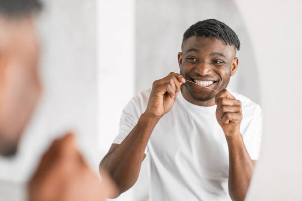 istock Smiling young black man flossing teeth near mirror in bathroom 2164537106
