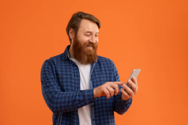 istock Cheerful redhaired man with beard smiles at his phone, studio 2164537120