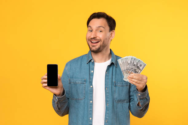 istock Man Holding Money and Cell Phone on Yellow 2164538023