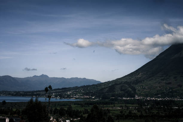 A serene view of an Andean lake with surrounding mountains in Ecuador, showcasing the tranquil waters and lush greenery under a clear blue sky.
