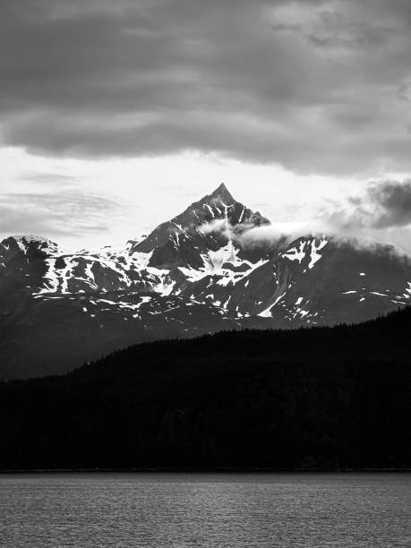 A serene view of Juneau, Alaska, featuring its calm waterfront, lush green forests, and snow-capped mountains in the background. This picturesque coastal town is surrounded by breathtaking natural beauty and offers a peaceful escape into the Alaskan wilderness.