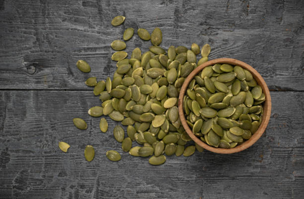 istock Bowl and Scattered Pumpkin Seeds on Rustic Wooden Surface 2164547798
