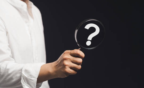istock Businessman holding a magnifying glass with a white question mark symbol while standing against a black background. 2164553180