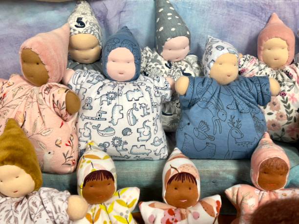 Horizontal closeup photo of a group of small dolls for young children crafted with a variety of skin coloured fabrics, natural fibre cotton and wool, using pastel coloured  patterned fabrics, on display for sale at a Waldorf Steiner school craft shop. Hobart, Tasmania