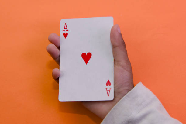 A hand holds up the Ace of Hearts playing card against a vibrant orange background, ready to play.