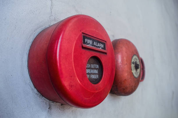 istock Retro fire alarm components attached to a white wall, such as a red break glass button and a bell. 2164567477
