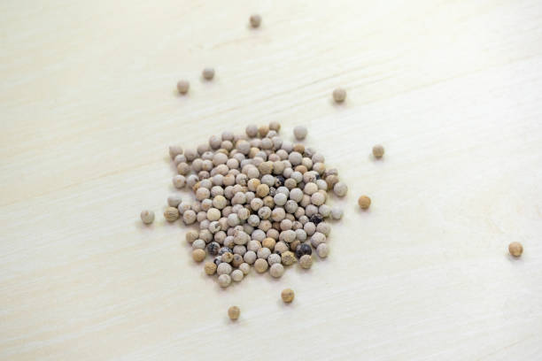 Dry white peppercorn (Piper nigrum) spice seeds on wooden background.