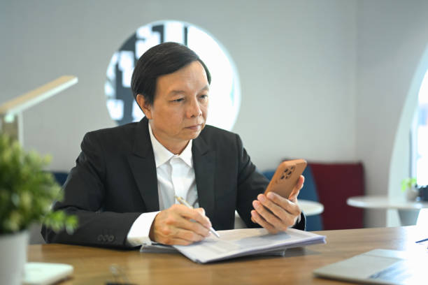 istock Middle aged businessman executive wearing suit using mobile phone in a modern office 2164576059