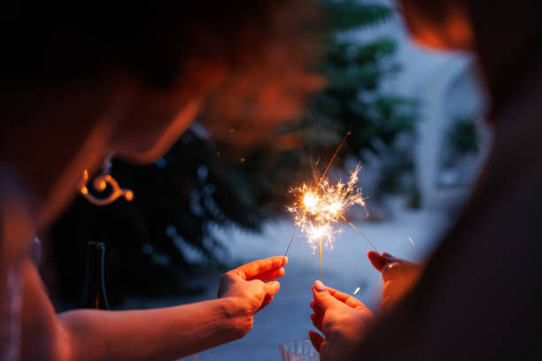 Two people holding sparklers, creating a festive atmosphere. The background is softly blurred with greenery, enhancing the celebratory mood.