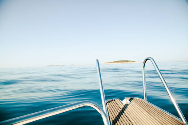 The surreal panoramic island view of Kornati Island National Park in Dalmatia (Croatia) on a clear blue summer day with a bit of morning haze and very calm tranquil sea, the front of a boat in the foreground. From a boat's perspective (boat trip).
