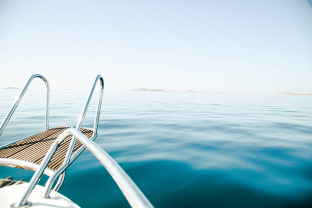 The surreal panoramic island view of Kornati Island National Park in Dalmatia (Croatia) on a clear blue summer day with a bit of morning haze and very calm tranquil sea, the front of a boat in the foreground. From a boat's perspective (boat trip).