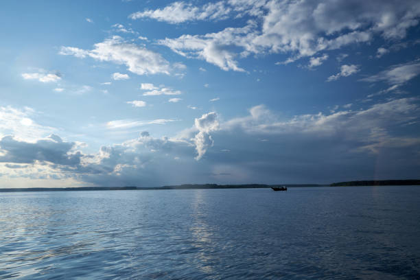 A boat sails down the river against a blue sky with clouds