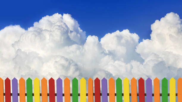 A Colorful Fence Against a Bright Blue Sky With Puffy Clouds