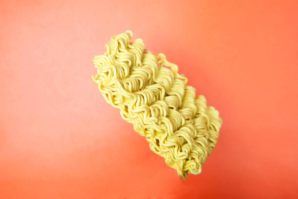A close up of a instant noodle. The noodle is long and thin, and it is sitting on a red background