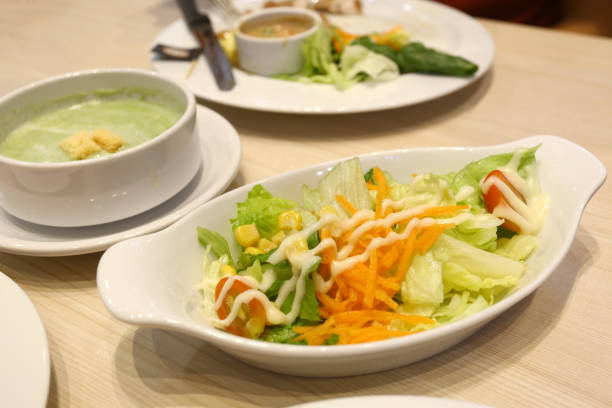 Tuna salad is served on a white plate on the dining table, and spinach soup is nearby.
