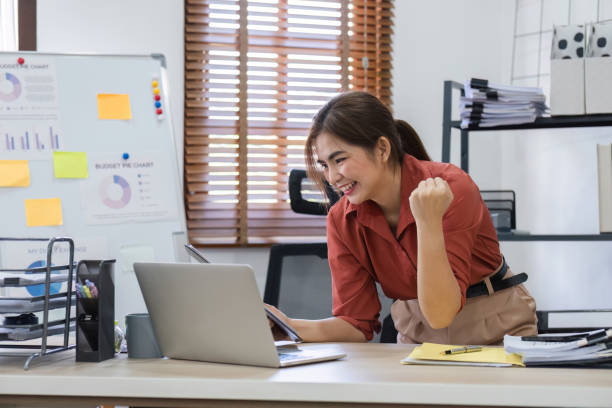 istock Successful Young Accountant Celebrates Her Work in Modern Office Environment with Laptop and Financial Charts 2164596418