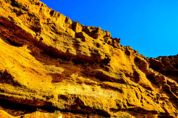 A rocky hillside with a blue sky in the background. The hill is covered in brown and yellow rocks