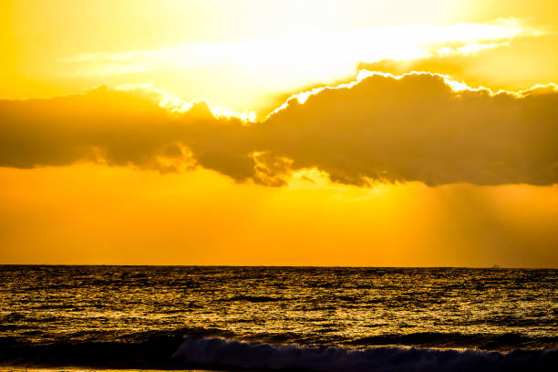 The sky is orange and the clouds are white. The sun is setting over the ocean. The water is calm and the sky is clear
