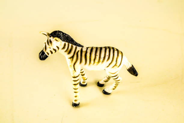 A zebra toy is sitting on a white surface. The toy is small and has a black and white striped pattern. The toy is placed in a way that it is looking at the camera. The image has a playful