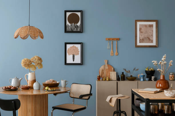 istock Dinning room and kitchen interior with mock up poster frame, round table, rattan chair, beige commode, vase with dried flowers, cup, pitcher and kitchen accessories. Home decor. Template. 2164604813