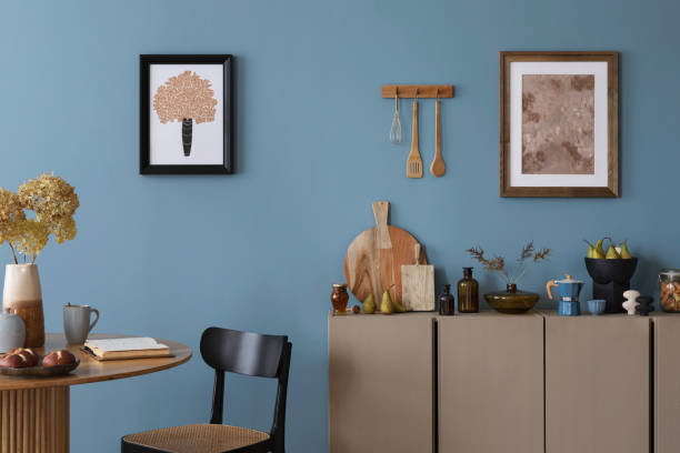 istock Dinning room and kitchen interior with mock up poster frame, round table, rattan chair, beige commode, vase with dried flowers, cup, pitcher and kitchen accessories. Home decor. Template. 2164604887