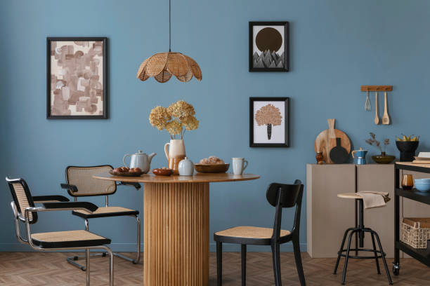 istock Interior design of warm dinning room interior with mock up poster frame, round table, rattan chairs, beige sideboard, stylish lamp, blue wall and personal kitchen accessories. Home decor. Template. 2164604891