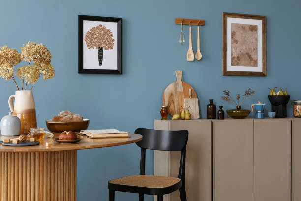 istock Warm and cozy dining room and kitchen interior with mock up poster frame, round table, rattan chair, beige commode, blue wall, vase with flowers and kitchen accessories. Home decor. Template. 2164604948