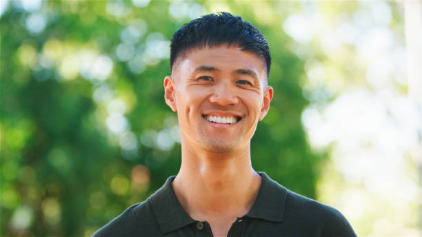 istock Young Man Smiling Outdoors Smiling To Camera in a Park on a Sunny Day Surrounded by Greenery 2164605847