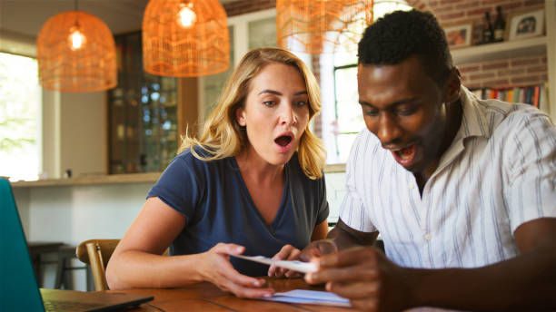 istock Surprised Couple Experiencing Excitement While Engaging With Mobile Device Indoors in Brightly Lit Room 2164606995