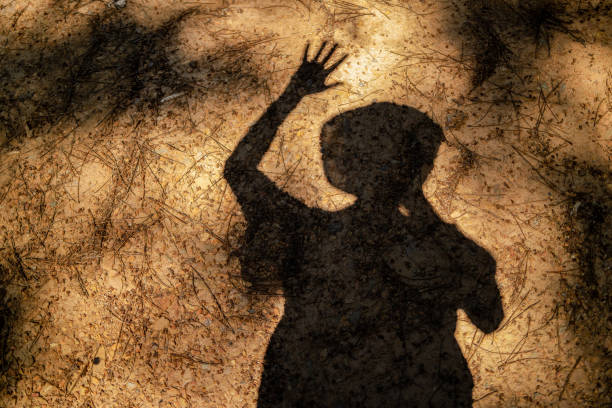 The shadow of a man raising a hand, projected on the ground covered with pine needles
