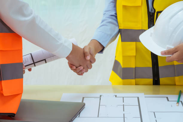 istock Two young women work at a desk, holding hands while designing and drawing plans for building a house. As architects construction contractors, meticulously plan every detail, including  house roof. 2164613964