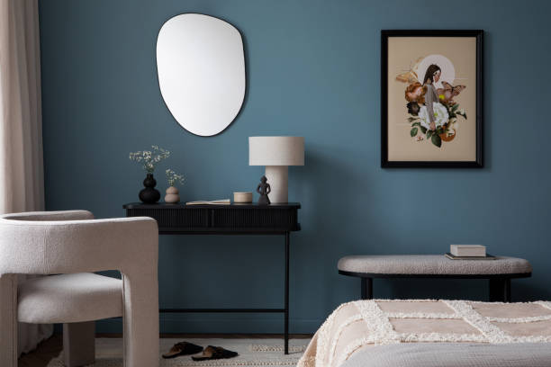 istock Creative composition of warm bedroom interior with mock up poster frame, blue wall, gray bedding, stylish armchair, bench, slippers, black desk, lamp and personal accessories. Home decor. Template. 2164615044