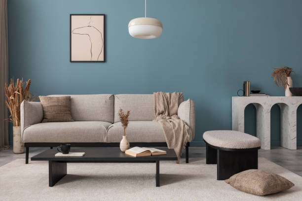 istock Warm and cozy blue room with mock up poster frame, cozy sofa, beige bedding, blue wall, pillows, wooden sideboard, bench, gray armchair, vase with flowers plants and personal accessories. Home decor. Template. 2164619196