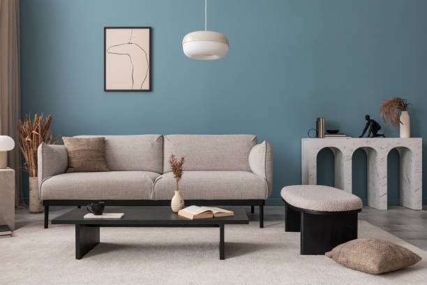istock Warm and cozy blue room with mock up poster frame, cozy sofa, beige bedding, blue wall, pillows, wooden sideboard, bench, gray armchair, vase with flowers plants and personal accessories. Home decor. Template. 2164619271
