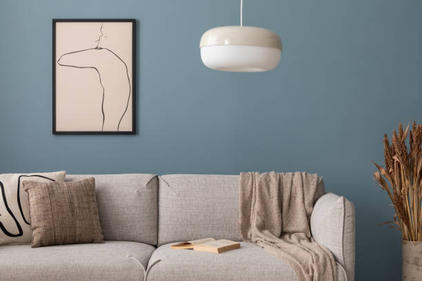istock Warm and cozy blue room with mock up poster frame, cozy sofa, beige bedding, blue wall, pillows, wooden sideboard, bench, gray armchair, vase with flowers plants and personal accessories. Home decor. Template. 2164619292
