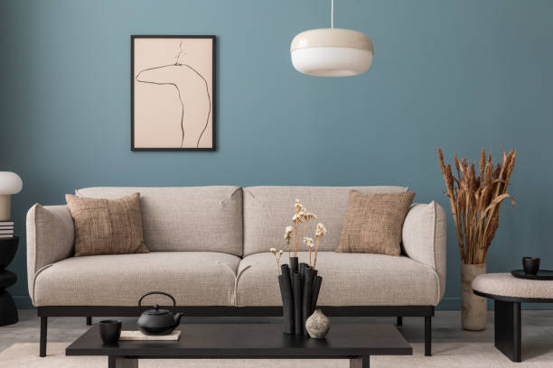 istock Warm and cozy blue room with mock up poster frame, cozy sofa, beige bedding, blue wall, pillows, wooden sideboard, bench, gray armchair, vase with flowers plants and personal accessories. Home decor. Template. 2164619295