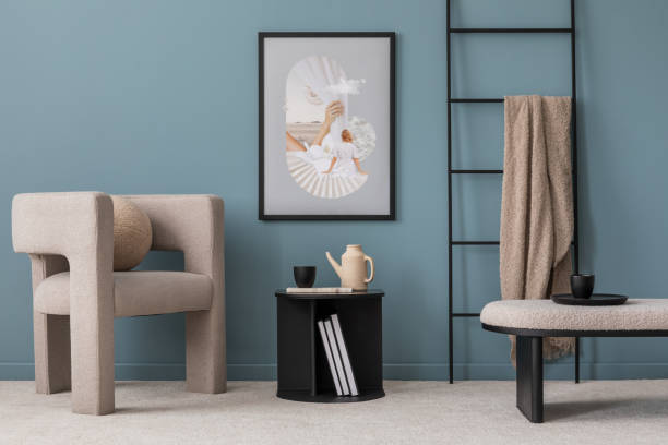 istock Warm and cozy blue room with mock up poster frame, cozy sofa, beige bedding, blue wall, pillows, wooden sideboard, bench, gray armchair, vase with flowers plants and personal accessories. Home decor. Template. 2164621287