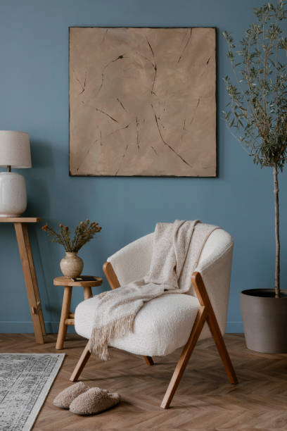istock Warm and cozy blue room with mock up poster frame, cozy sofa, beige bedding, blue wall, pillows, wooden sideboard, bench, gray armchair, vase with flowers plants and personal accessories. Home decor. Template. 2164626506