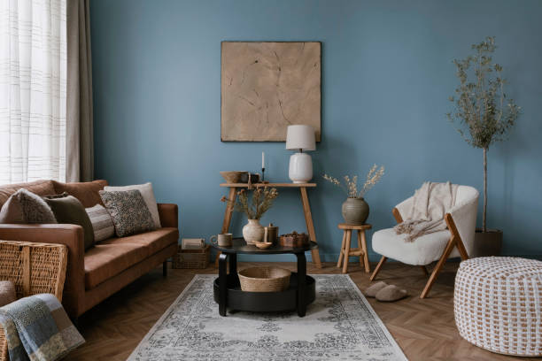 istock Warm and cozy blue room with mock up poster frame, cozy sofa, beige bedding, blue wall, pillows, wooden sideboard, bench, gray armchair, vase with flowers plants and personal accessories. Home decor. Template. 2164626510