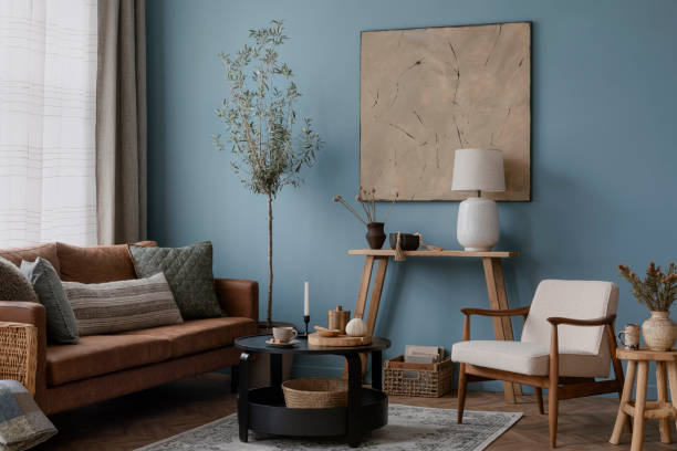 istock Warm and cozy blue room with mock up poster frame, cozy sofa, beige bedding, blue wall, pillows, wooden sideboard, bench, gray armchair, vase with flowers plants and personal accessories. Home decor. Template. 2164626517