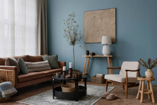 istock Warm and cozy blue room with mock up poster frame, cozy sofa, beige bedding, blue wall, pillows, wooden sideboard, bench, gray armchair, vase with flowers plants and personal accessories. Home decor. Template. 2164626567