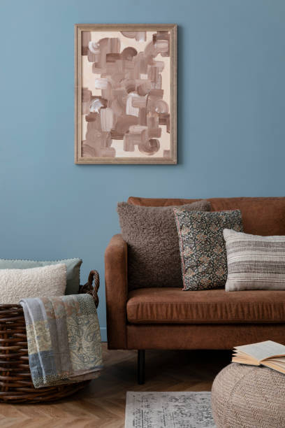 istock Warm and cozy blue room with mock up poster frame, cozy sofa, beige bedding, blue wall, pillows, wooden sideboard, bench, gray armchair, vase with flowers plants and personal accessories. Home decor. Template. 2164626580