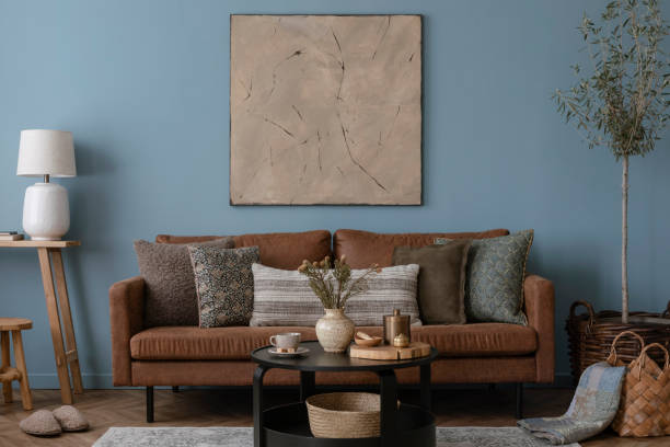 istock Warm and cozy blue room with mock up poster frame, cozy sofa, beige bedding, blue wall, pillows, wooden sideboard, bench, gray armchair, vase with flowers plants and personal accessories. Home decor. Template. 2164626610