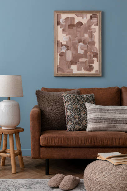 istock Warm and cozy blue room with mock up poster frame, cozy sofa, beige bedding, blue wall, pillows, wooden sideboard, bench, gray armchair, vase with flowers plants and personal accessories. Home decor. Template. 2164626677