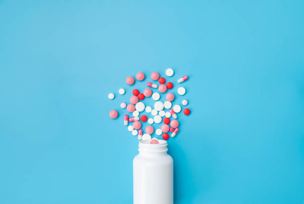 istock Multi-colored tablets, pills, capsules, vitamins spilling out of white plastic container on blue background, flat lay top view. Concept of medicine, health care, pharmaceuticals 2164633519